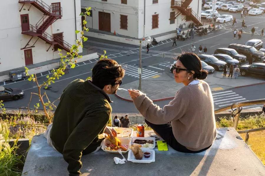 一对夫妇在贝博体彩app梅森堡中心露天用餐. 女人让她的伴侣尝尝食物.