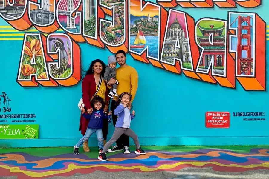 Uma família posando para uma foto em frente a um mural de São Francisco